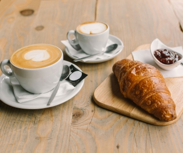 A wooden table with a latte and croissant